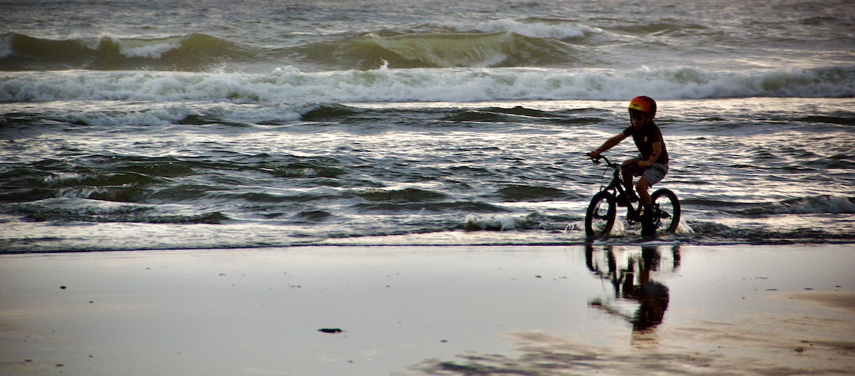 boy bicycling at surf's edge