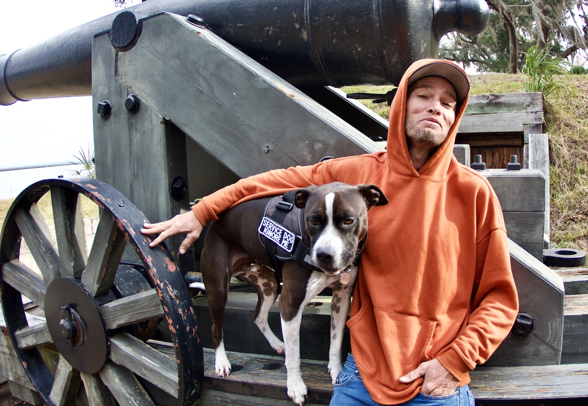 man and dog sit on a cannon