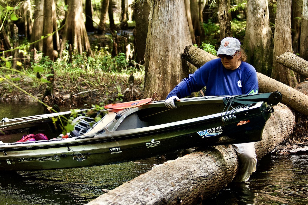 kayaker slides boat over tree across river